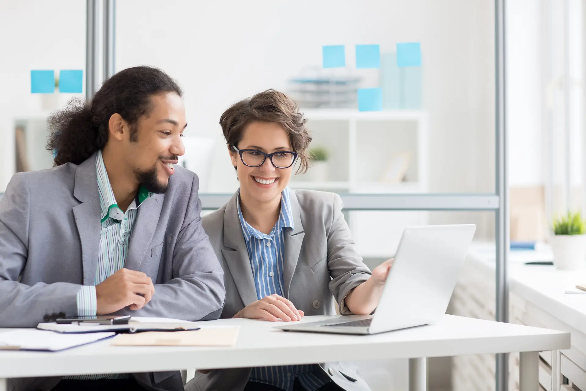 Confident and friendly analyst pointing at laptop display while explaining data to colleague